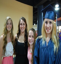 A girl in a graduation cap and gown surrounded by her friends
